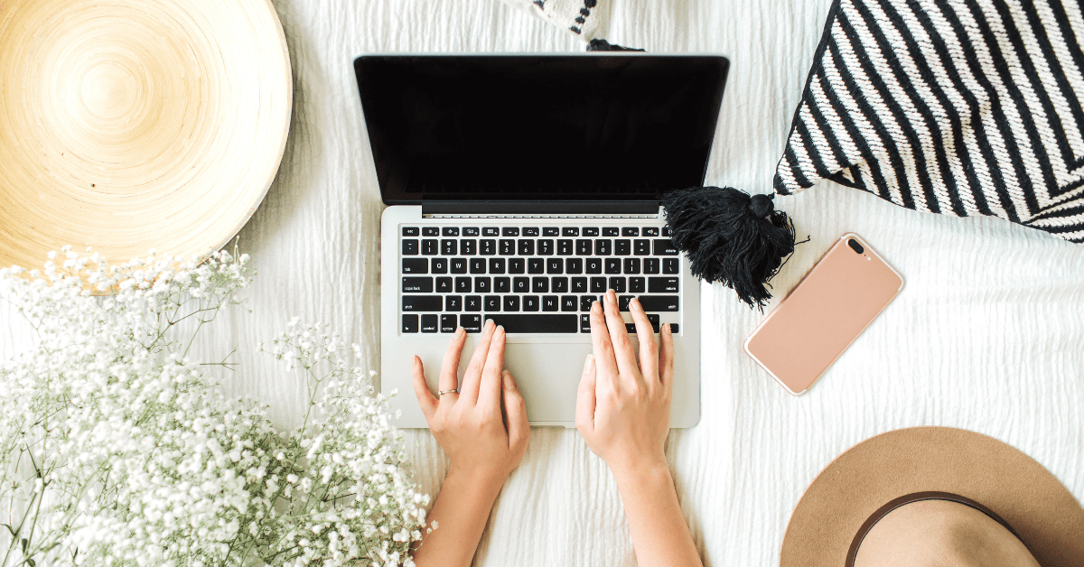 Bird's-eye view of a woman on a laptop on a bed next to a smartphone.