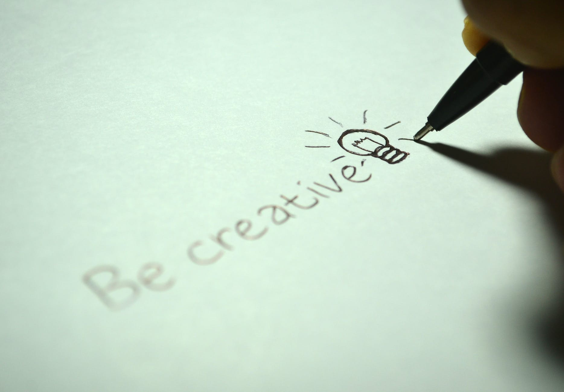 A person writing the words be creative on a piece of paper.
