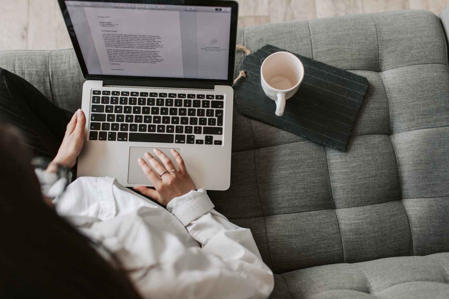 Woman using a laptop on the sofa at home next to an empty coffee cup.
