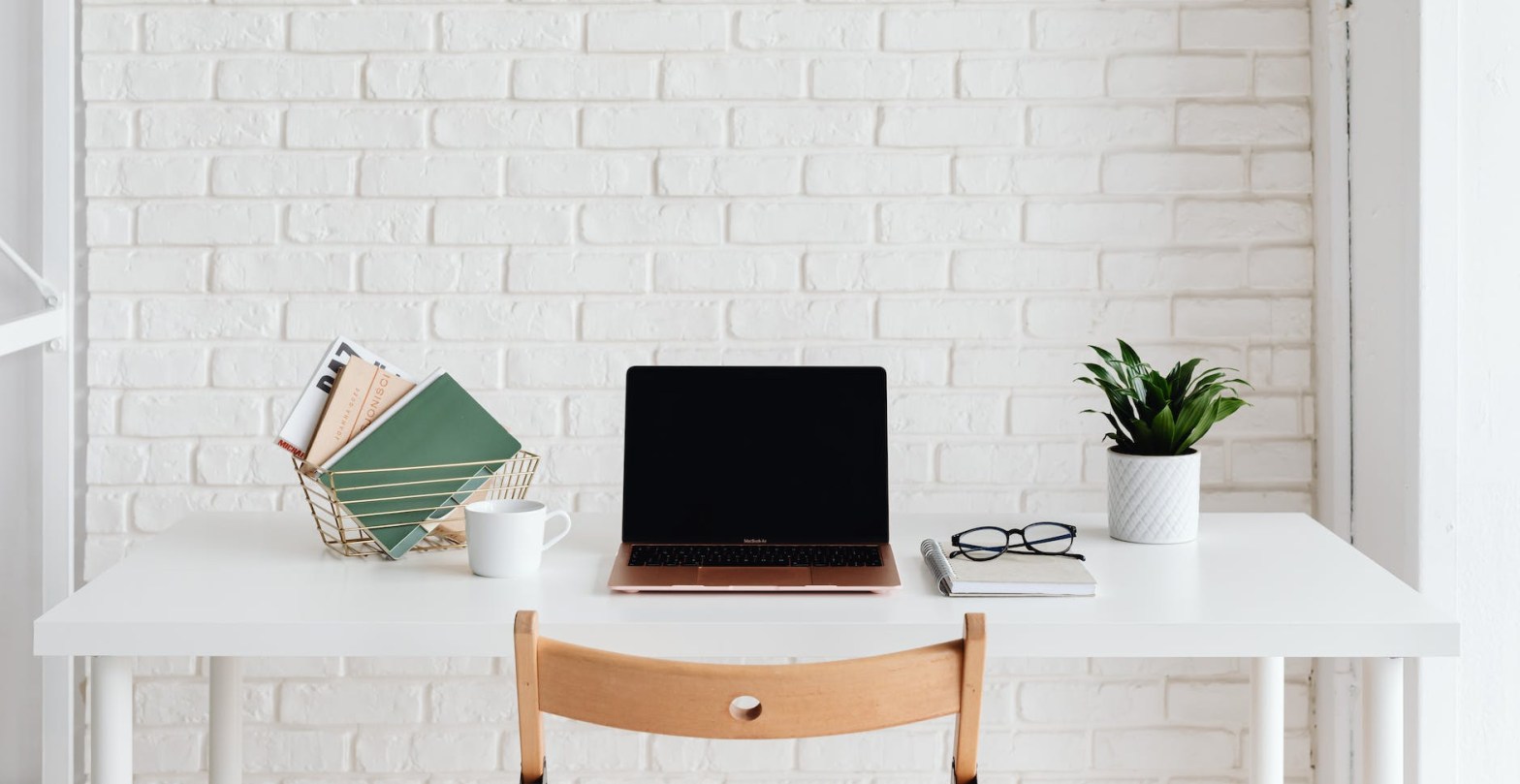 Laptop on white desk beside white brick wall.